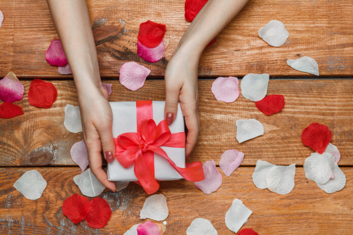 Valentines Day gift and Female hands on wooden background with petals